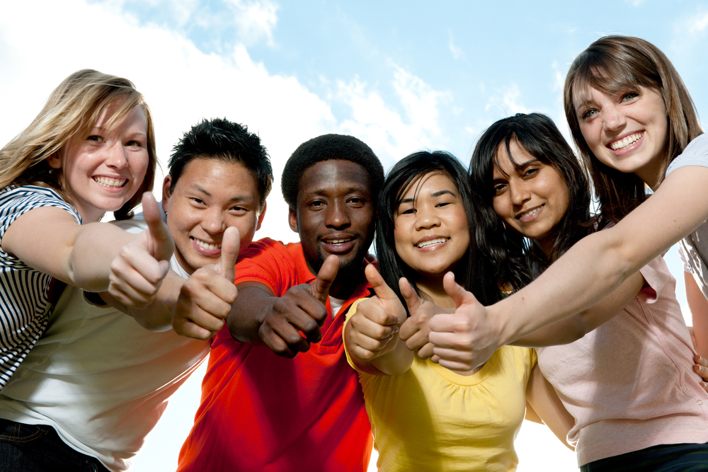 Diverse group of young Black, Asian and white people smiling and giving a thumbs up